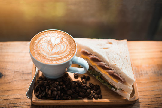A cup of coffee with heart pattern in a white cup and Sandwich on wooden table background - Image