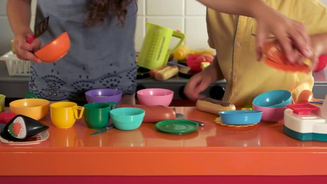 Close up kids playing in a toy kitchen. Children playing with plastic tableware at home or daycare center. Activity center for children.