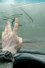 the human hand fingers drawing lines on a sweaty moisture from the inside glass of the car in rainy weather