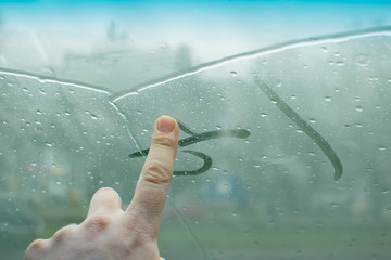 the human hand fingers drawing lines on a sweaty moisture from the inside glass of the car in rainy...