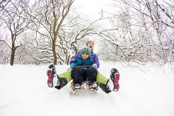 A woman with her son rides down the hill in a sleigh and screaming.