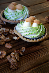 On the wooden table are cakes with protein cream, similar to baskets of mushrooms. Nearby are peeled walnuts. Work days of rustic pastry