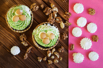 Cake with cream, similar to the baskets with mushrooms, walnuts and meringues on the table of pine planks. Brown and pink background. View from above