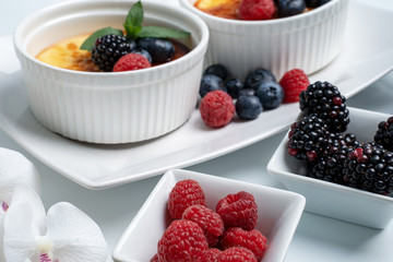 Creme Brulet in weißen Schalen mit Himbeeren und Brombeeren