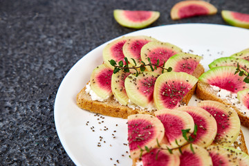 Healthy breakfast toasts from sliced watermelon radish or chinese daikon, chia and cottage cheese on black background. Copy space.
