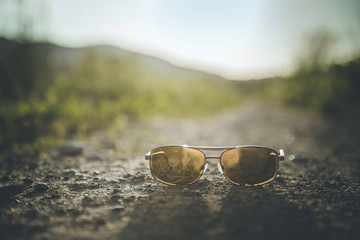 Fototapeta na wymiar Summer holiday adventure concept: sunglasses are lying on the floor of a country road, close up