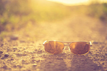 Fototapeta na wymiar Summer holiday adventure concept: sunglasses are lying on the floor of a country road, close up