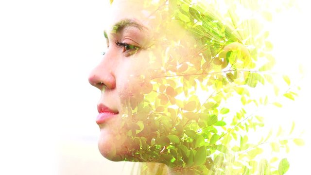 Double exposure video of green leaves in the wind passing over close up of peaceful woman