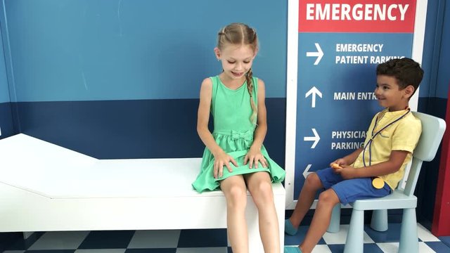 Little doctor neurologist examining female patient. Kid playing doctor role game examining girl patient using reflex hammer sitting in playroom at entertainment center.