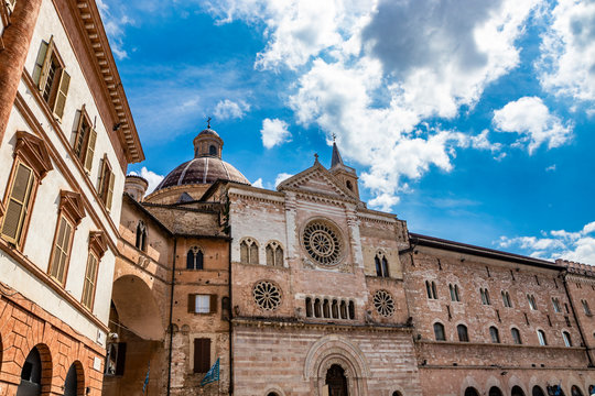 The Cathedral of San Feliciano in the square of Foligno. The side facade, with 3 rosettes, mullioned windows, arches and columns. The bell tower, the dome and the wooden portal. Perugia, Umbria, Italy