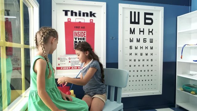 Little girls playing doctor and patient indoor. Happy kid with stethoscope and syringe making an injection to her patient. Healthcare and childhood concept.