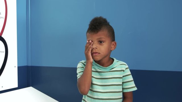 Doctor ophthalmologist checks vision of child boy. Little boy covering one eye with hand. Child at eye sight test.