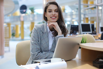 Portrait of a cheerful young businesswoman sitting at the table in office and looking at camera.