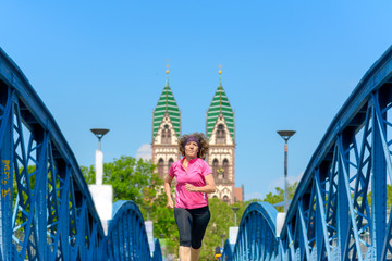 Smiling woman jogging across an urban bridge