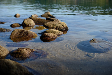 Wet pebbles on seashore in evening sun light. Sea wave on seacoast with round stones.