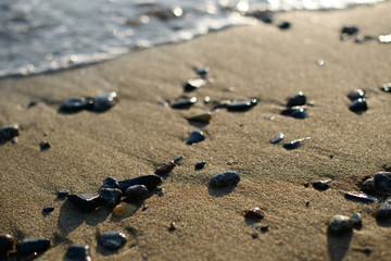 Wet pebbles on seashore in evening sun light. Sea wave on seacoast with round stones.