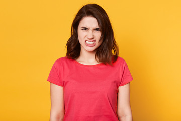 Obraz premium Image of annoyed angry model having unpleasant facial expression, looking dangerously, setting teeth, wearing red casual item of clothes, being in irritating mood. People and emotions concept.