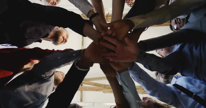 Close-up happy diverse adult business people joining hands together. Team spirit at modern multiethnic loft office.