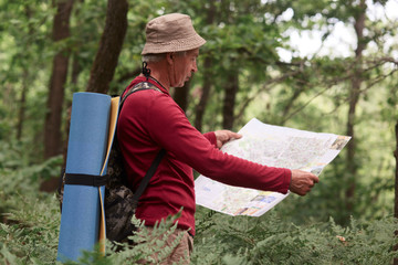 Image of old man traveling, having active rest, spending his vocation backpacking, standing with map, tries to find right way. Traveling, active recreation, adventure, spending time in open fresh air.