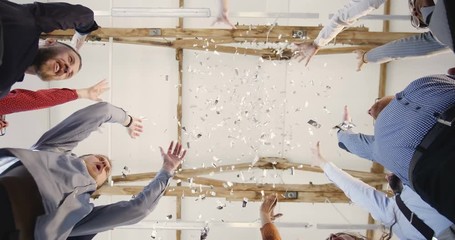 Close-up happy multiethnic group of business people joining hands together, clapping under confetti at office background