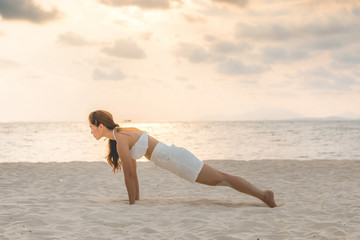 Fototapeta na wymiar Asian young woman practice yoga Plank or Phalakasana Pose on the sand and beach with sunset beautiful sea in Tropical island,Feeling comfortable and relax in holiday,Vacations Yoga Concept