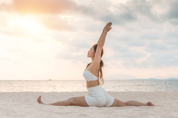 Fototapeta na wymiar Asian young woman practice Yoga Monkey God Pose or Yoga Hanumanasana pose on the sand and beach with sunset beautiful sea in Tropical island,Feel comfortable and relax in holiday,Vacation Yoga Concept