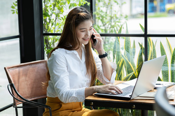 Beautiful Attractive Asian woman working with laptop smile and talking with customer in smartphone to get idea and requirement for success job outside office in coffee shop,Business Concept