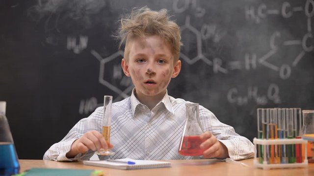 Shocked funny dirty schoolboy holding chemical tube and flask, smoke around him