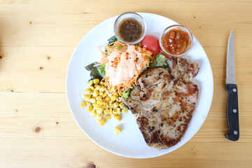 pork chop steak and salad with black pepper sauce and chili sauce on white  dish and wood table with knife, left copy space