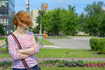 A red-haired, informally-dressed middle-aged woman with freckles stands in a strong wind with her face covered by hair