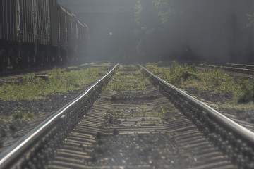 Fototapeta premium An empty railroad line with a freight train standing on a side track covered by smoke.