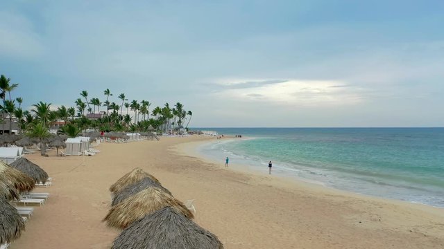Sandy palm beach along the Atlantic coast. Endless turquoise ocean with white waves in cloudy weather. White sunny sand against the background of bright blue water.