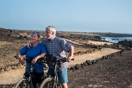 Two bikers with e bike stop to rest after a long excursion on the footpath Couple of senior people man and woman standing on the cliff. Healthy lifestyle for two retired persons enjoying bicycles. 
