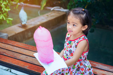 Close up portrait of the little girl in the floral pattern, holding a pink cotton swab in the hand, happily at amusement park