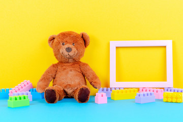 Baby kids toys background with empty picture frame, teddy bear and colorful building blocks bricks