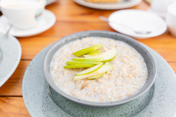 Breakfast and coffee in the summer cafe. Fresh oatmeal porridge with apples, honey, nuts and cinnamon close up for healthy breakfast