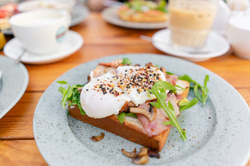 Breakfast and coffee in the summer cafe. Sandwich on a bun brioche with bacon, mushrooms, arugula and poached egg