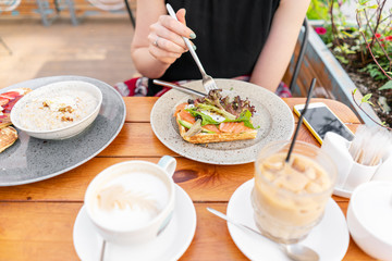 Traditional Belgian waffle with salmon, lettuce leaves and poached egg. A young woman is having Breakfast in a summer cafe, hands with a fork and a knife close-up. Cold coffee with ice cubes