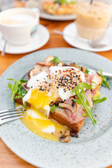 Breakfast and coffee in the summer cafe. Sandwich on a bun brioche with bacon, mushrooms, arugula and poached egg