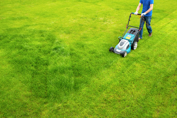 A lawn mower is cutting green grass, the gardener with a lawn mower is working in the backyard, a...