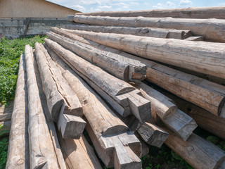 A pile of logs in the open air against the sky and a barn.