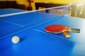 Two rackets for a table tennis or Ping-Pong and a ball on a blue table.