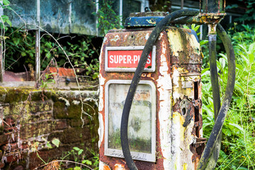 Rotting and rusty old gas fuel petrol pump abandoned in an overgrown yard beside a derelict building