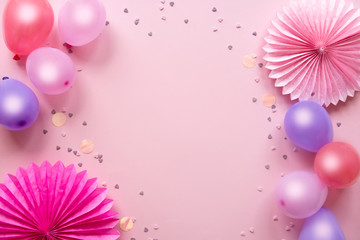 Colorful balloons and confetti on pink table top view. Birthday, holiday or party background. Flat lay style. Empty space for text. Festive greeting card.