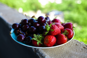 Organic sweet cherry and strawberry on a white plate.