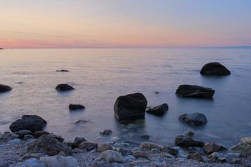 Fototapeta na wymiar sunset in the sea with black rocks in the front. long shutter time. blurry sea with red sky