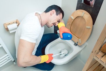 Man is a bit disgusted cleaning the toilet