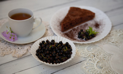 chocolate cake slice with a white cup of tea and a handful of currants