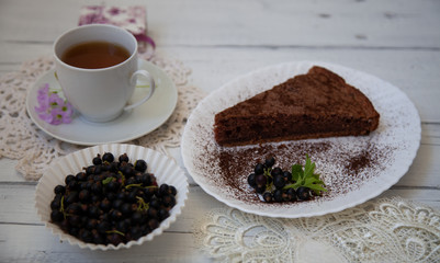 chocolate cake slice with a white cup of tea and a handful of currants