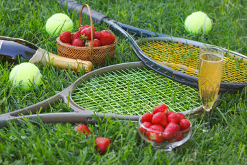 Strawberries with whipped cream, glass with champagne and tennis rackets and balls on grass. Wimbledon Grand slam tennis concept.